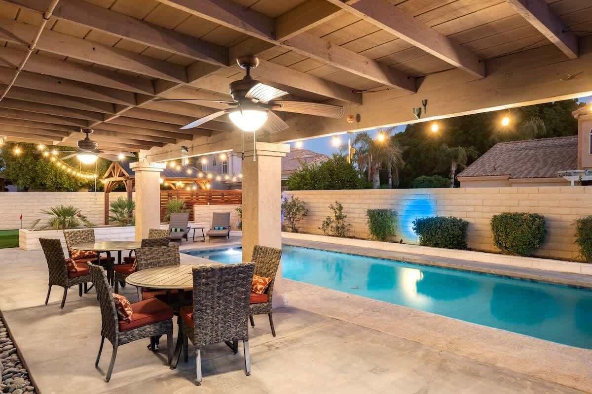 An outdoor pool area with a covered patio, seating, and a ceiling fan.