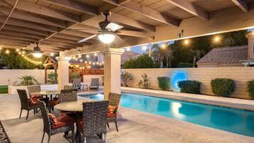 An outdoor pool area with a covered patio, seating, and a ceiling fan.