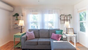 A living room with a sofa, two lamps, a small table, and a window with curtains.