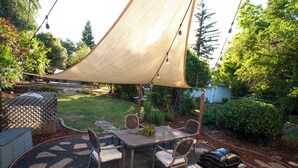 An outdoor patio with a table and chairs, a barbecue grill, and a large shade sail.