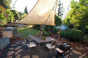 An outdoor patio with a table and chairs, a barbecue grill, and a large shade sail.