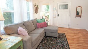 A living room with a sectional sofa, a patterned rug, a small table, and a door with a frosted glass window.