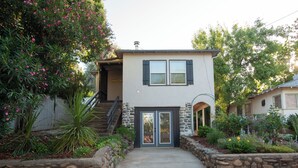 A two-story house with a stone pathway leading to the front door, surrounded by lush greenery and flowering plants.