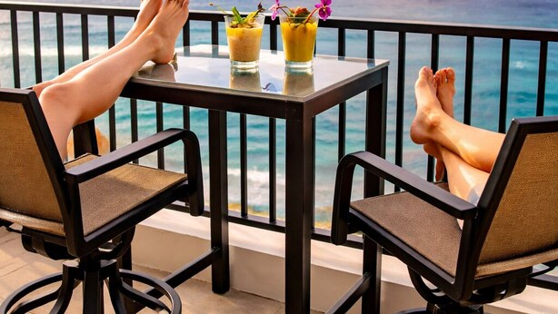 Two people seated at a table with drinks, overlooking a scenic ocean view with a rainbow.