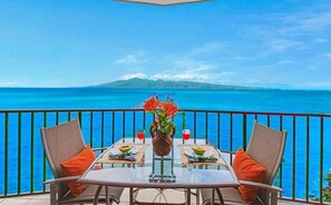 Une table avec des chaises et un vase de fleurs sur un balcon donnant sur l’océan.