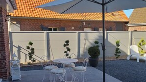 Eine Terrasse mit Tisch und Stühlen, einem weißen Sonnenschirm und einer weißen Bank.