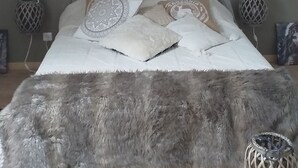 Ein gemütliches Schlafzimmer im Loft-Stil mit schrägverdeckter Decke, einem großen Bett mit gemusterten Kissen, einem hängenden Traumfänger und einem rustikalen Kronleuchter.