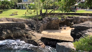 Um imóvel costeiro com área de natação definida, escadas de pedra que levam a um alpendre e um jardim exuberante.