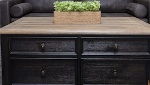 A dark brown leather sofa with a woven basket containing green plants on a wooden coffee table. Below the sofa is a dark wooden dresser with two drawers. - Quiet and cozy new townhome minutes from the mall exit. (Barboursville)