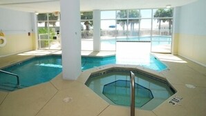 An indoor swimming pool with a hot tub, clear glass walls, and a view of the outside. - 3BR Fort Morgan Condo | Pool & Hot Tub (GULF SHORES)