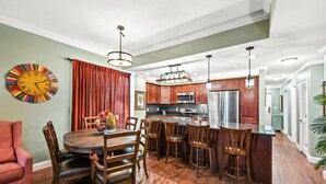 A spacious kitchen with wooden cabinets, a central island, and a dining area with a round table and chairs. - 3BR Fort Morgan Condo | Pool & Hot Tub (GULF SHORES)