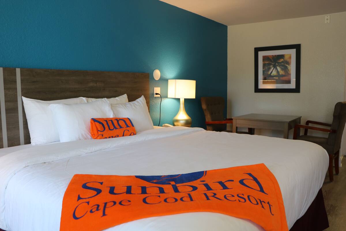 A hotel room with a bed, a desk, a chair, and a wall-mounted lamp.