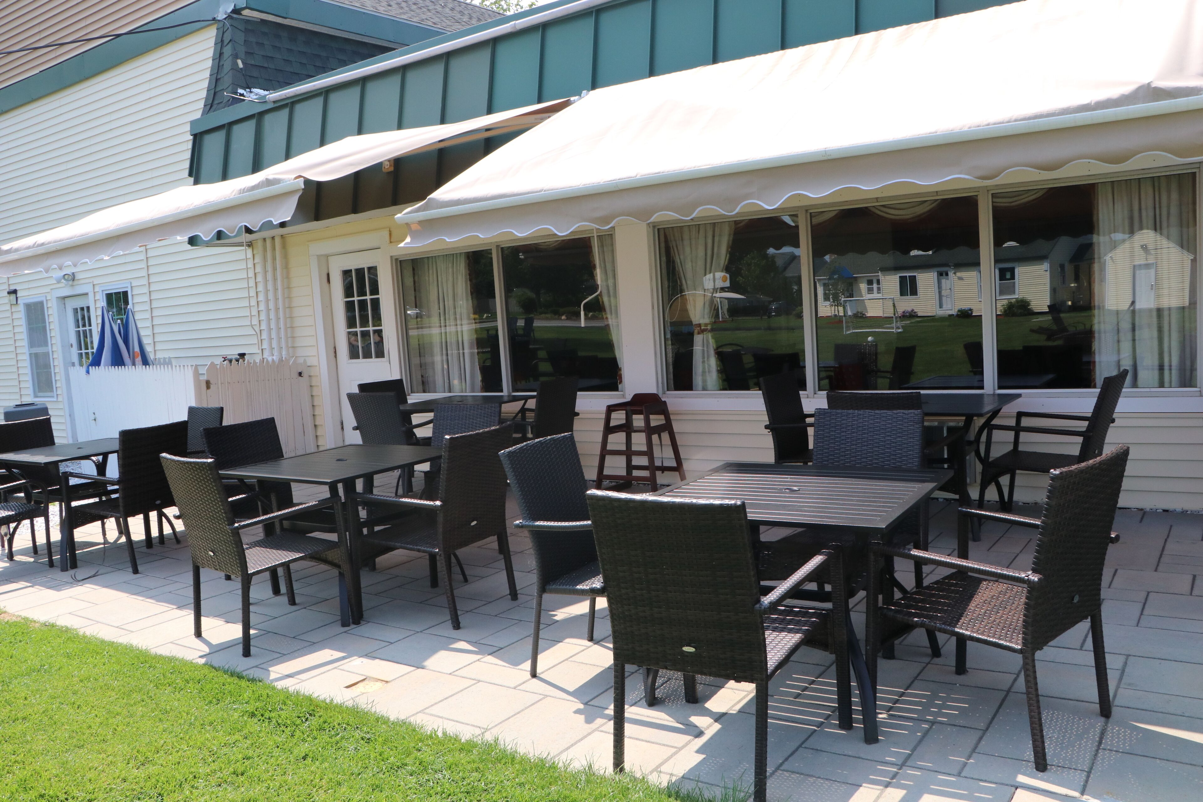 An outdoor patio with tables and chairs, a covered seating area, and a view of a house in the background.