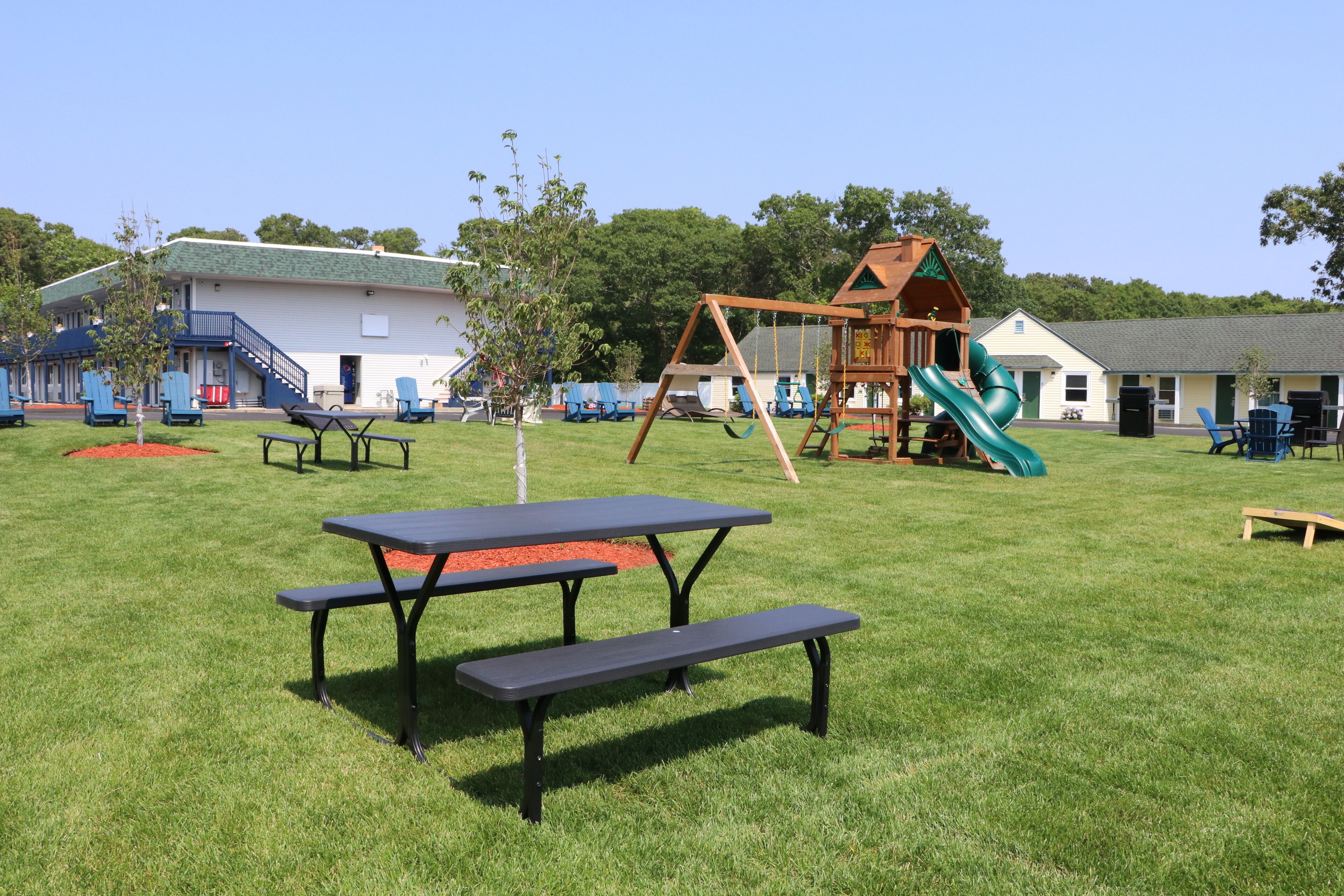 A playground with a swing set and slide, picnic tables, and a building with a green roof.