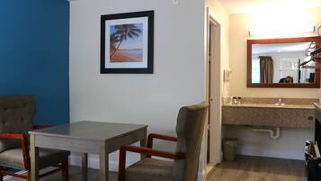 A hotel room with a dining area, a bathroom with a sink, and a framed picture of a beach scene.