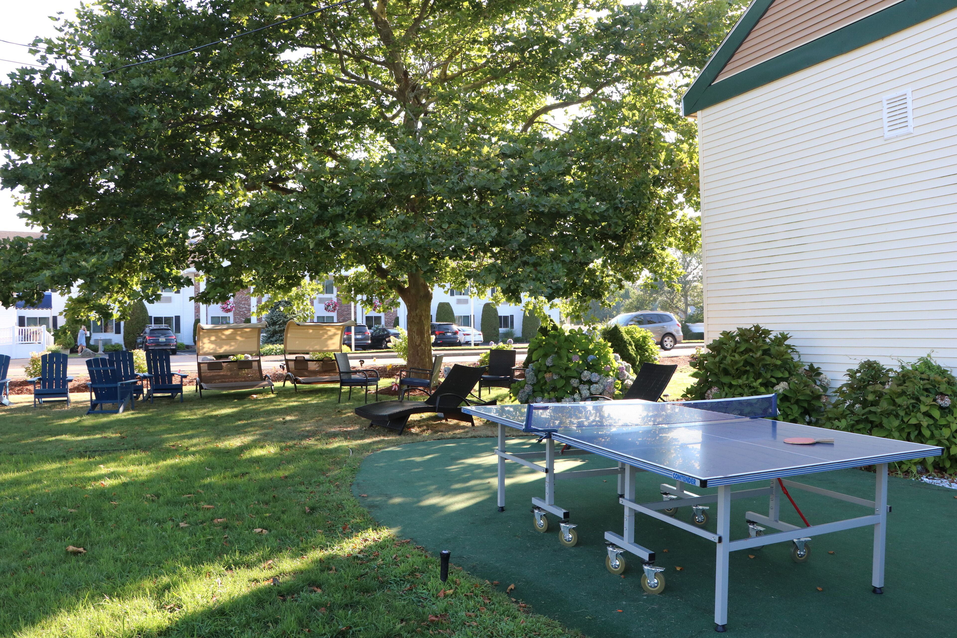 A ping pong table in a grassy outdoor area with chairs and a white building in the background.
