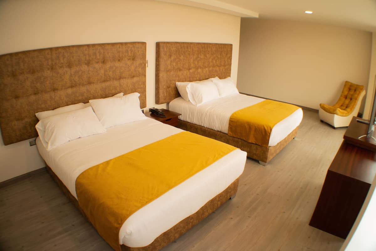 A hotel room with two beds, a chair, and a wooden desk.
