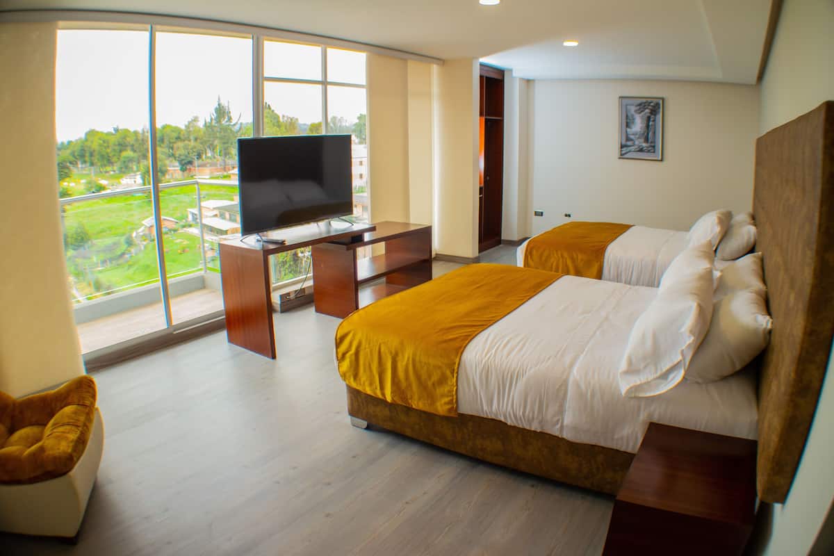 A hotel room with a large window, a bed, a desk with a TV, and a chair.