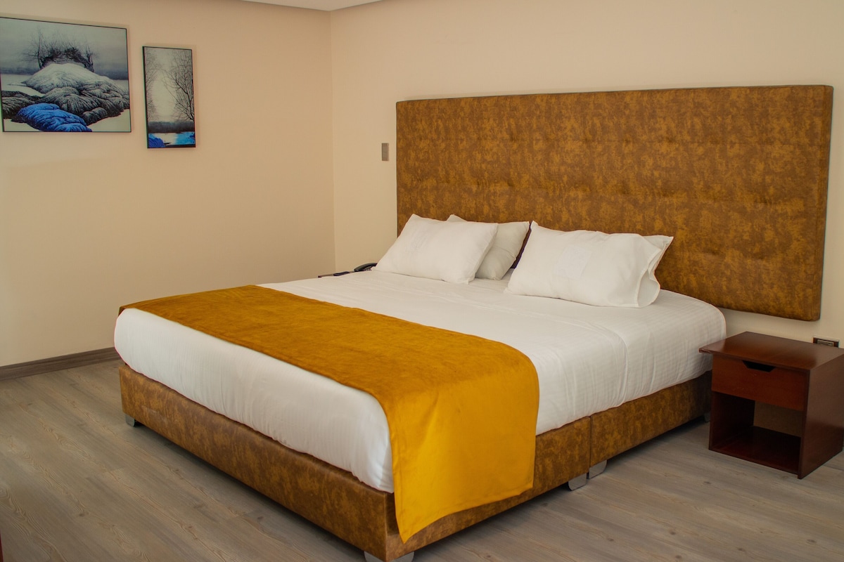 A hotel room with a large bed, a wooden headboard, a bedside table, and two paintings on the wall.