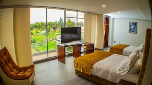 A modern hotel room with a large window, a TV on a wooden stand, two beds, a brown chair, and a wardrobe. - Harmony Hotel (Ipiales)