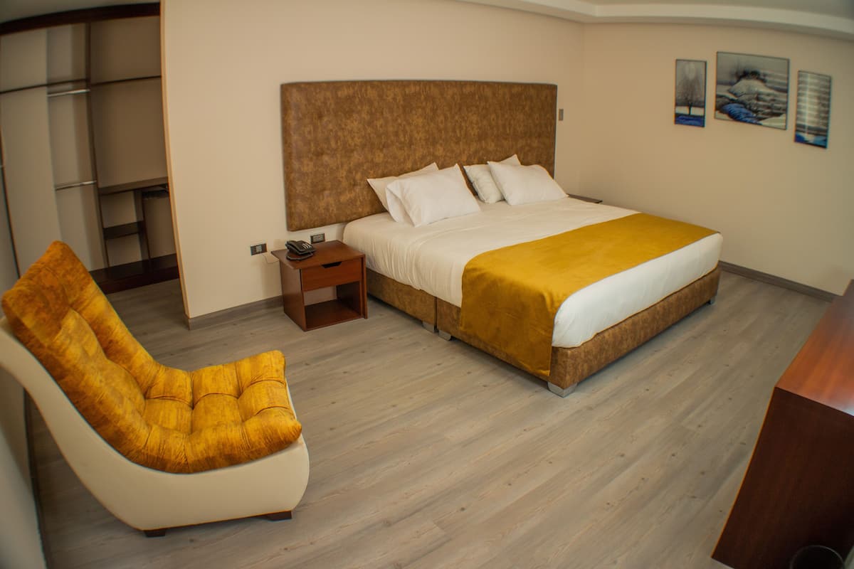 A hotel room with a bed, a bedside table, a chair, and a wardrobe.