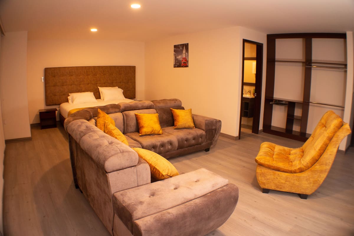 A modern hotel room with a large bed, a sofa, a chair, and a small table.