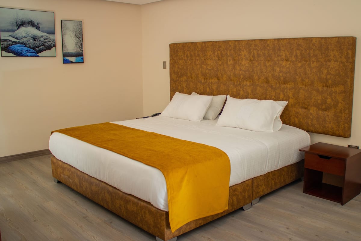A large bed with a wooden headboard, white bedding, and a mustard-colored throw blanket. There is a wooden nightstand beside the bed.