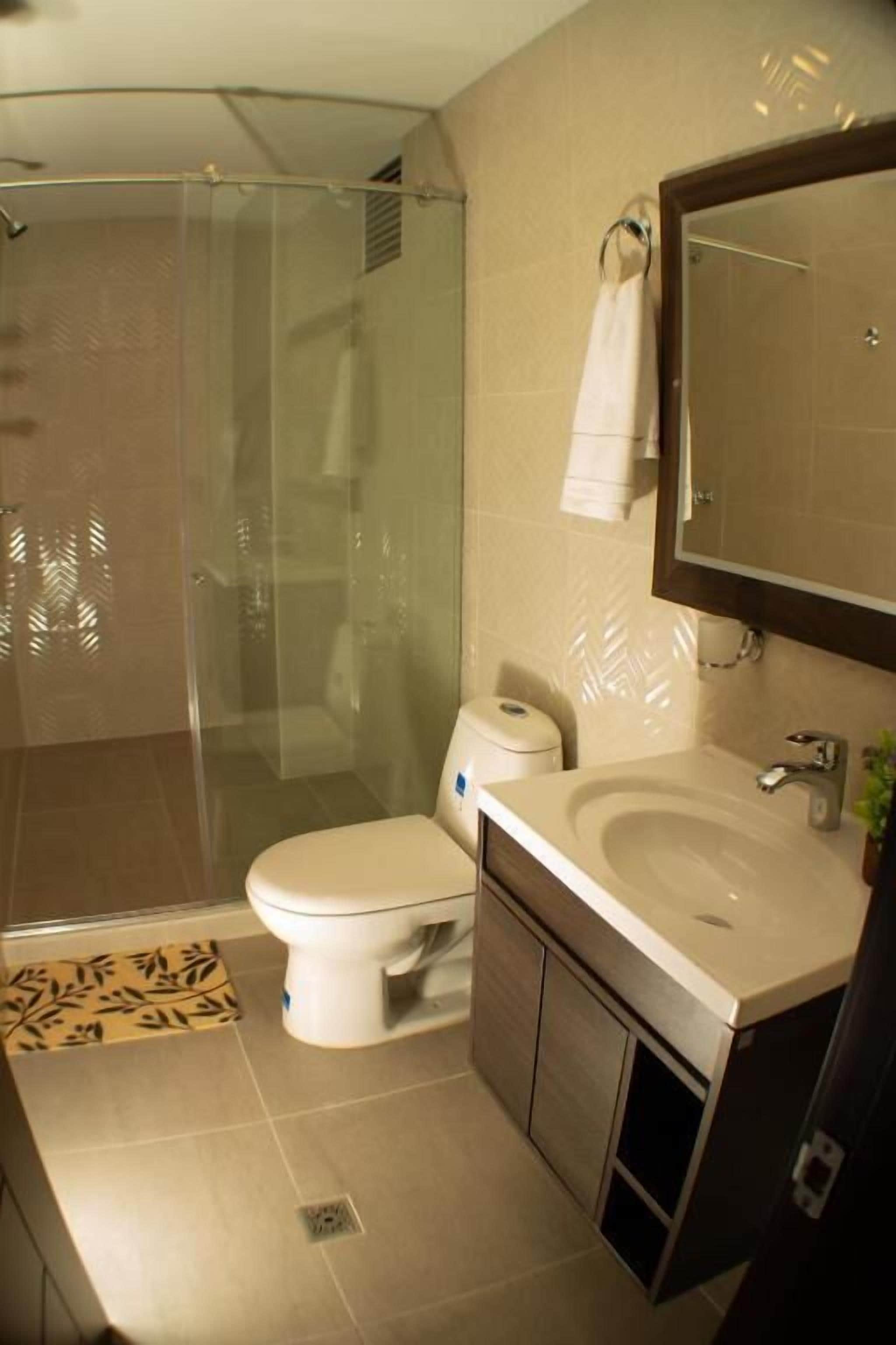 Une salle de bain moderne avec une douche à parois de verre, des toilettes et un lavabo surmonté d’un miroir.