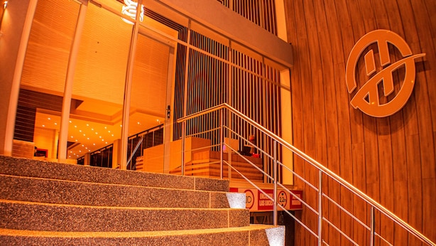 A staircase leading to a second floor with a wooden wall and a large logo. - Harmony Hotel (Ipiales)