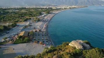 An aerial view of a coastal area with a beach, parking lot, and buildings in the background.