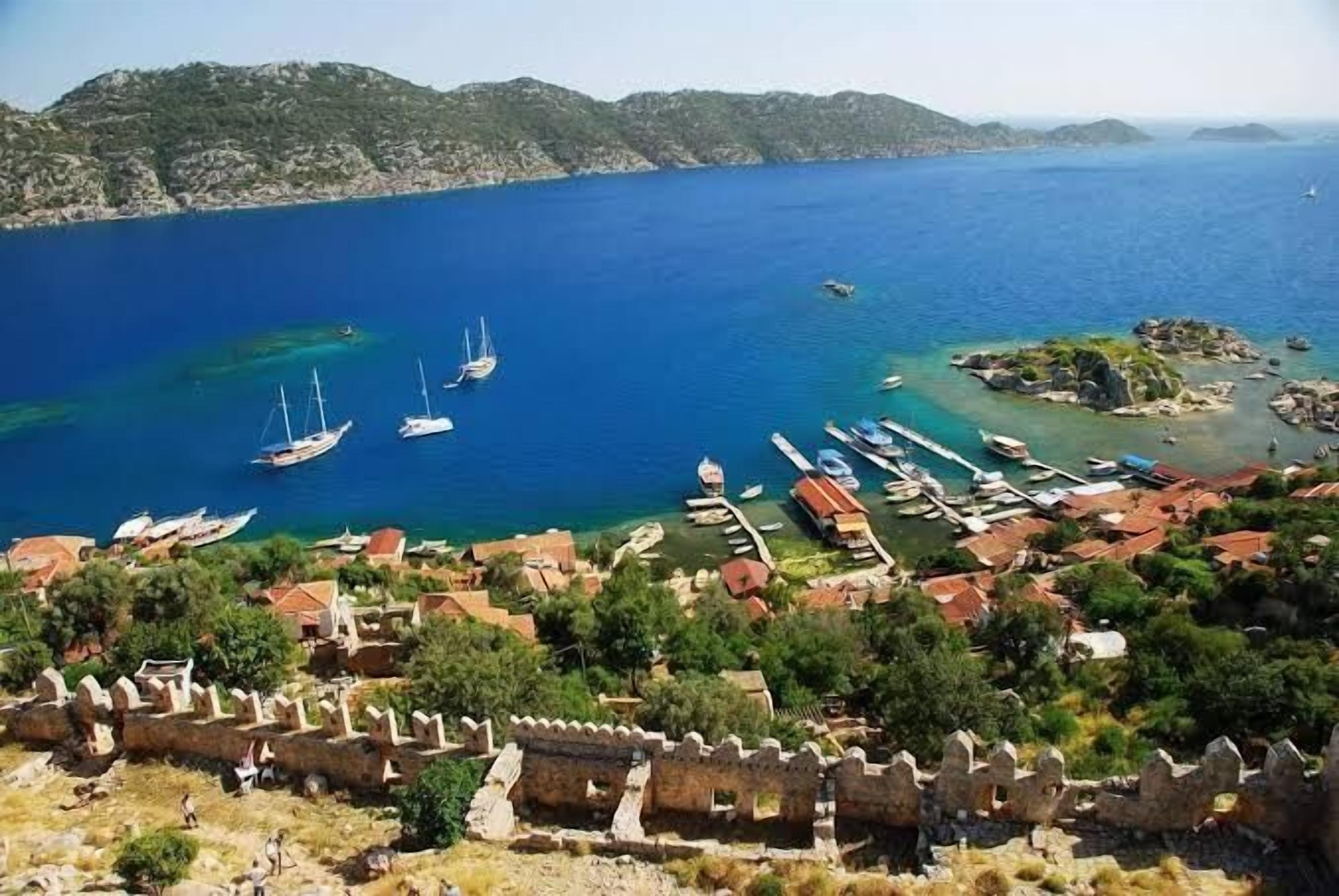 Un pueblo costero con una fortificación histórica, aguas azules cristalinas y barcos amarrados en el puerto deportivo.