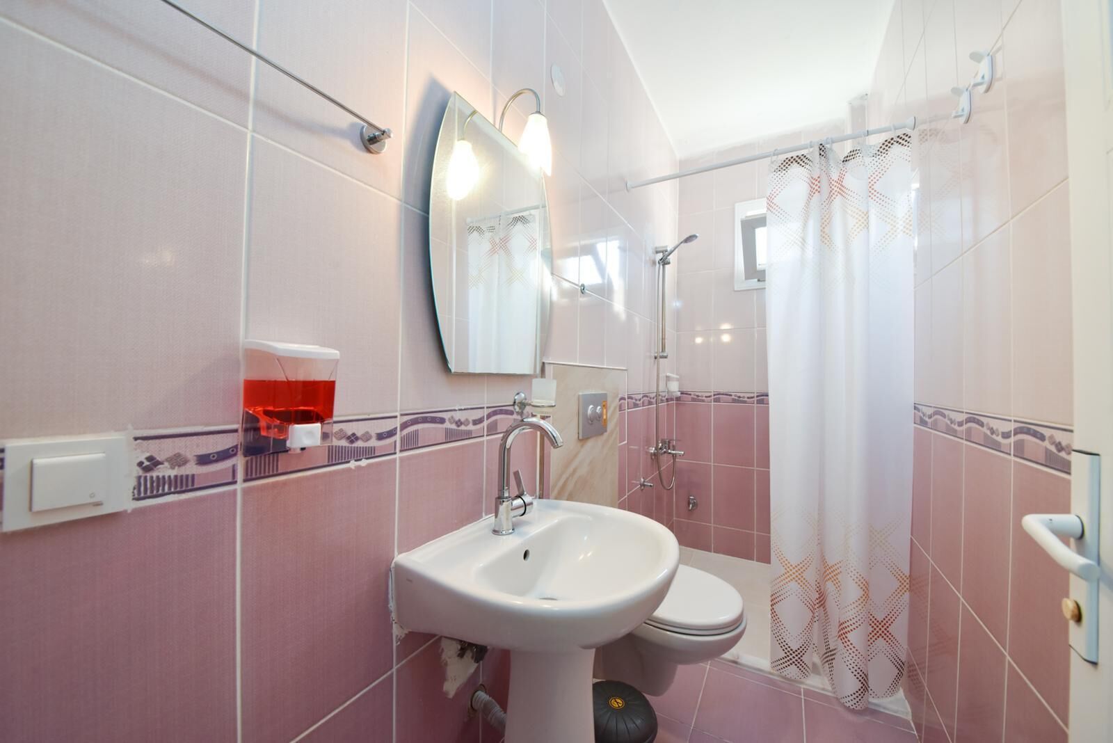 Une salle de bain équipée d’un lavabo, d’un miroir, d’une douche et de toilettes.