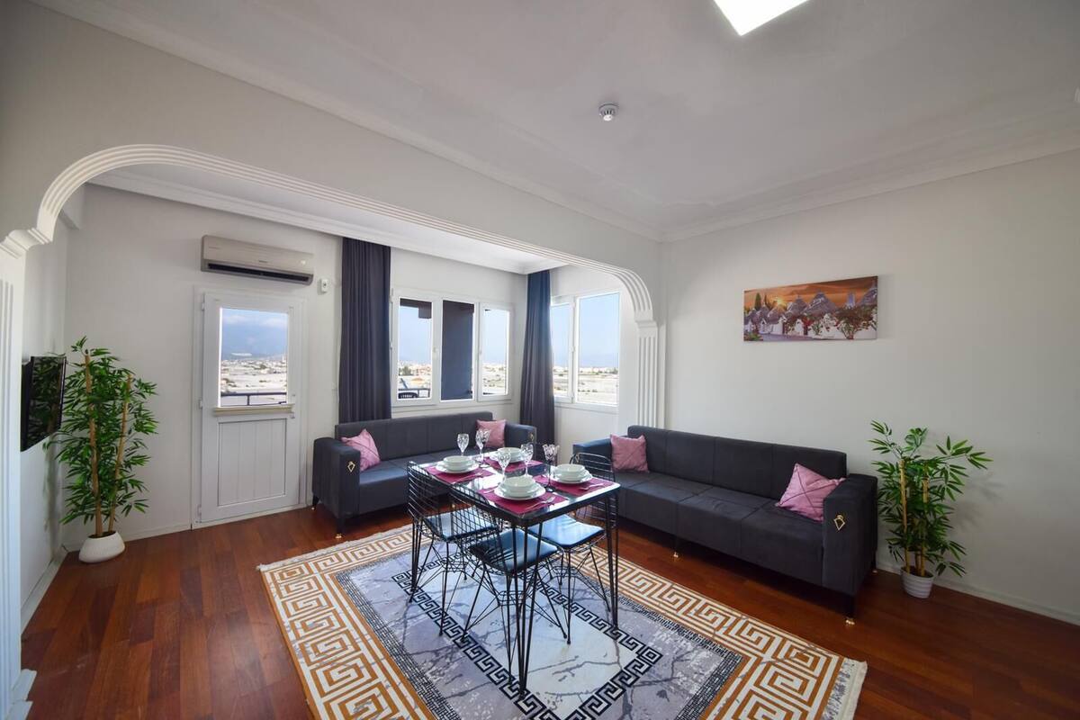A modern living room with a sofa, a dining table set for two, and a view of the city through large windows.