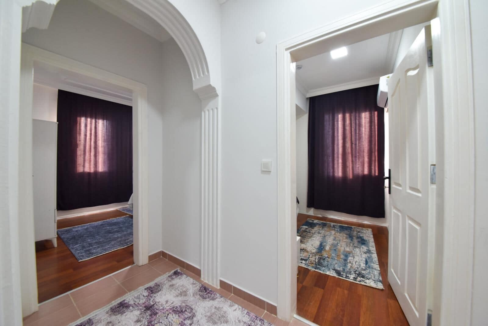 Un pasillo con dos puertas, cada una que da a una habitación con cortina oscura y una alfombra estampada en el suelo.
