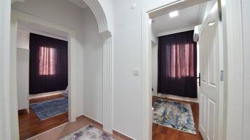 Un pasillo con dos puertas, cada una que da a una habitación con cortina oscura y una alfombra estampada en el suelo.