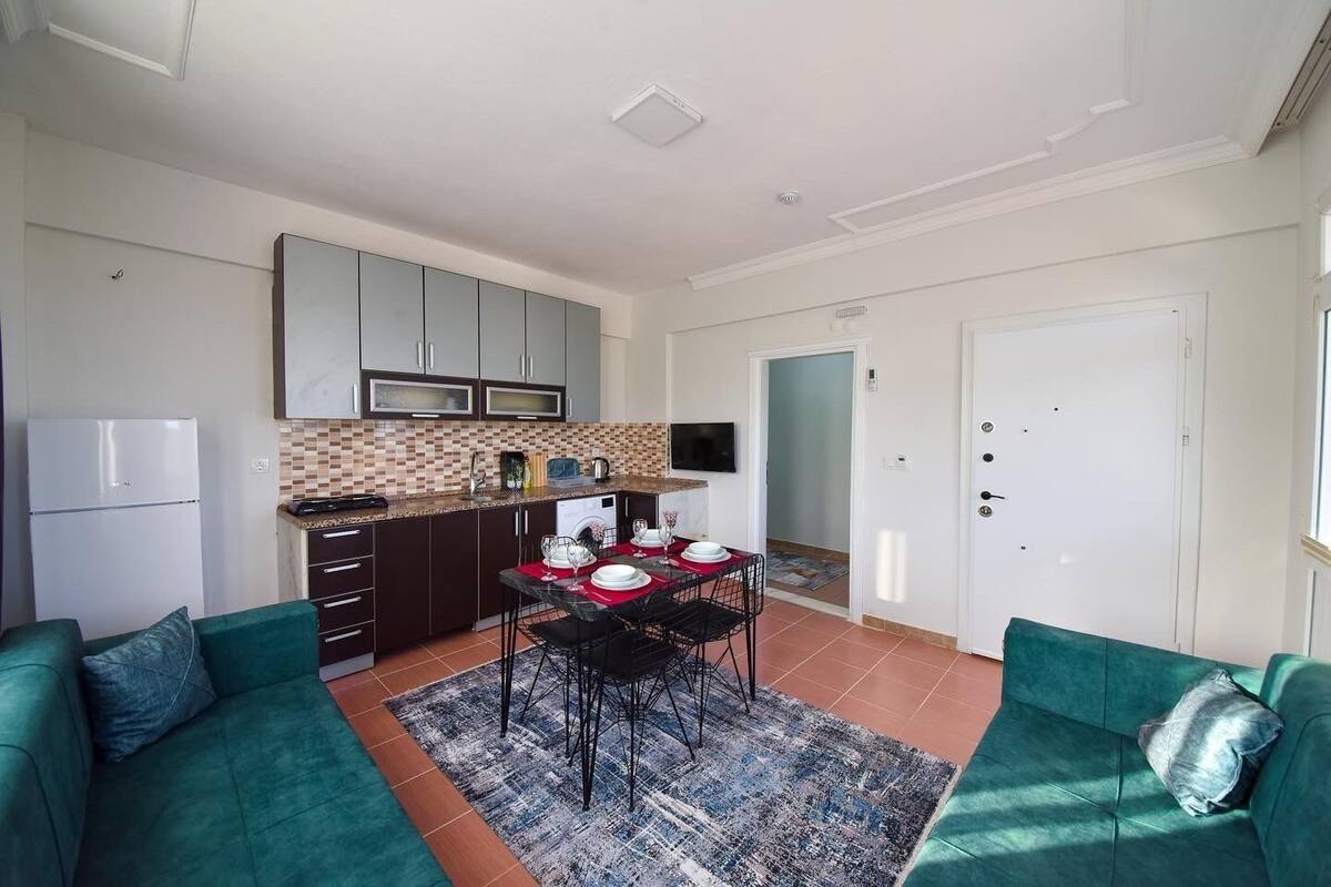 A compact living space with a kitchenette, dining area, and two green sofas.