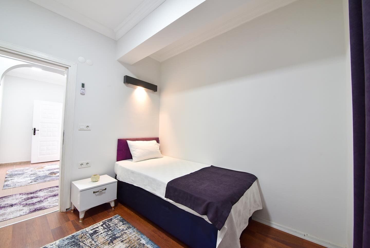 Une chambre à coucher avec un lit, une table de chevet et une commode. Il y a une porte qui donne sur une autre pièce et une fenêtre avec vue.