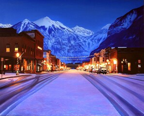 A snow-covered street with buildings on either side and a mountain in the background.
