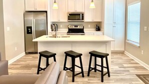 Una cocina moderna con armarios blancos, un refrigerador de acero inoxidable, un microondas, una estufa y tres taburetes negros.
