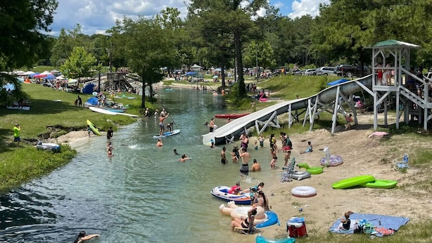 Un río con gente disfrutando de actividades acuáticas, un parque infantil y un área de picnic.