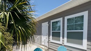 Un patio con dos sillas Adirondack turquesa, una palmera, y una casa con contraventanas blancas y revestimiento exterior gris.
