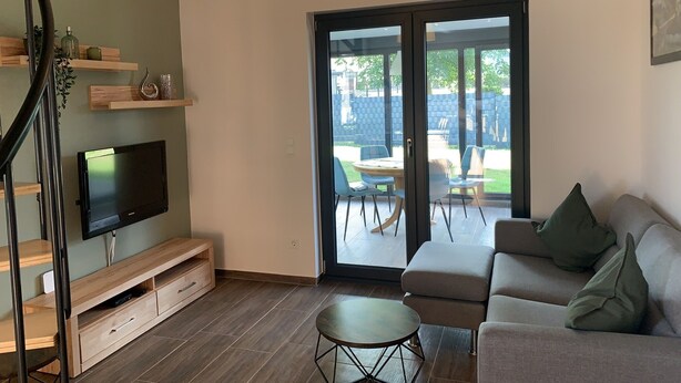 A modern living room with a flat-screen TV, wooden shelves, a sofa, and a dining area with chairs. - Feel-good accommodation, starting point for mountain bike tours and hikes (Höhn)