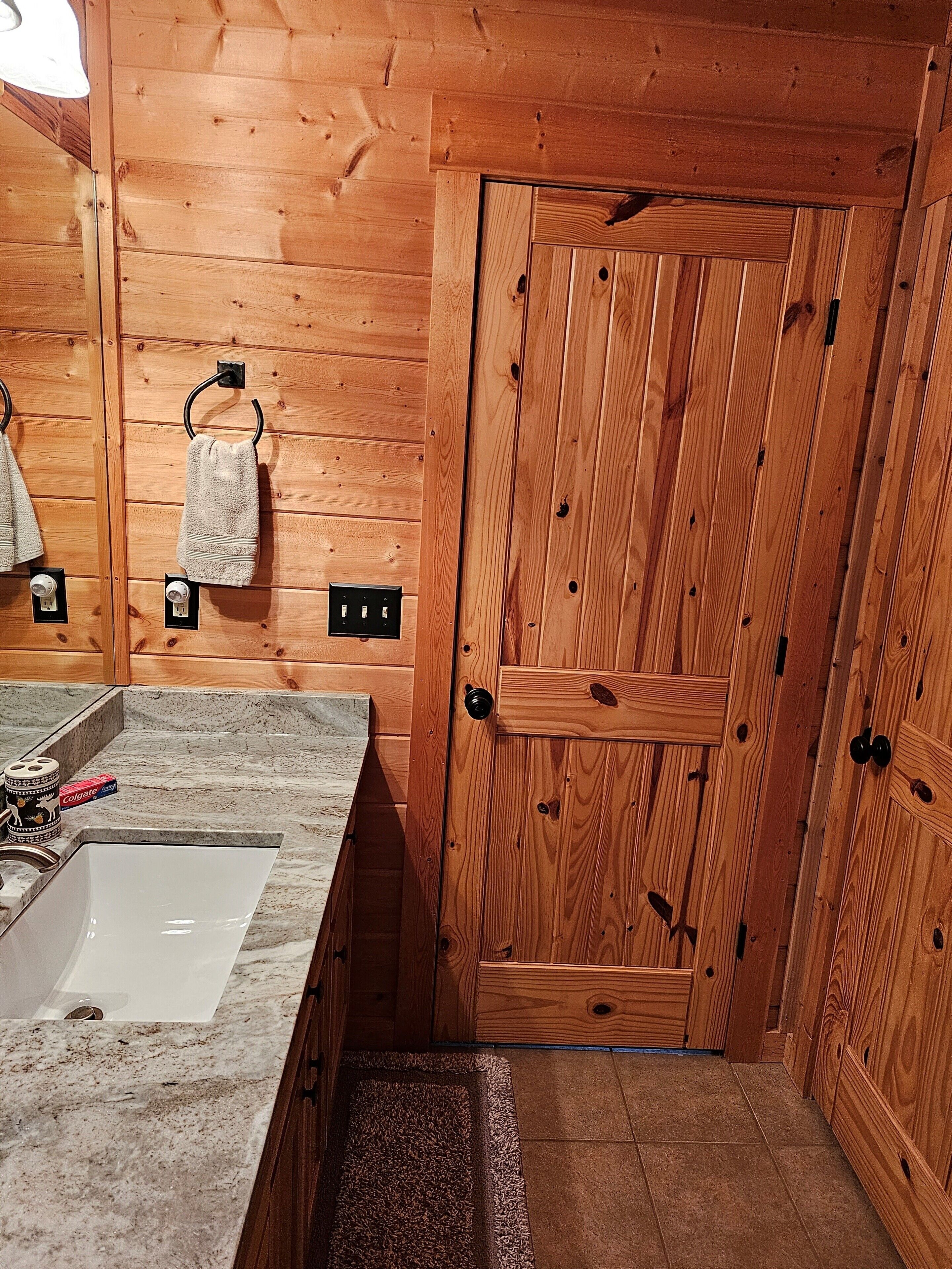 Une salle de bain en bois comprenant un lavabo, un miroir, un porte-serviettes et une porte.