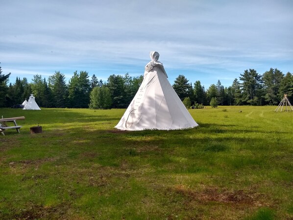 A tent-like structure in a grassy field with trees in the background. - North Woods 12' Teepee Resort (Exeter)