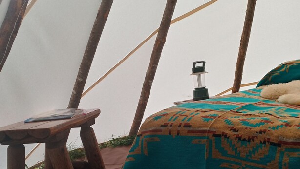 A tent with a bed, a small wooden table, and a lantern. - North Woods 12' Teepee Resort (Exeter)