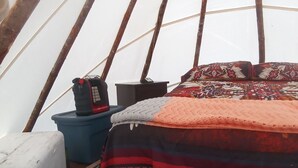 A tent with a bed, a small table, and a white object on the floor. - North Woods 12' Teepee Resort (Exeter)