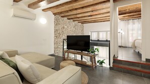 A living room with a TV on a wooden stand, a stone wall, and a staircase leading to a bedroom. - OLA LIVING MACBA 0 (Barcelona)
