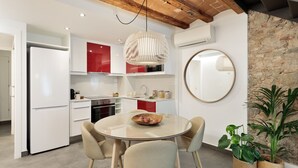 A modern kitchen with white cabinets, a red accent wall, a round dining table with four chairs, and a hanging light fixture. - OLA LIVING MACBA 0 (Barcelona)