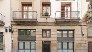 A two-story building with a ground-floor garage door, a balcony with a metal railing, and a small window with a security camera. - OLA LIVING MACBA 0 (Barcelona)