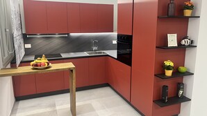 A compact kitchen with red cabinetry, a black countertop, and a small wooden table with fruit. - TWO-ROOM APARTMENT (Porto San Giorgio)